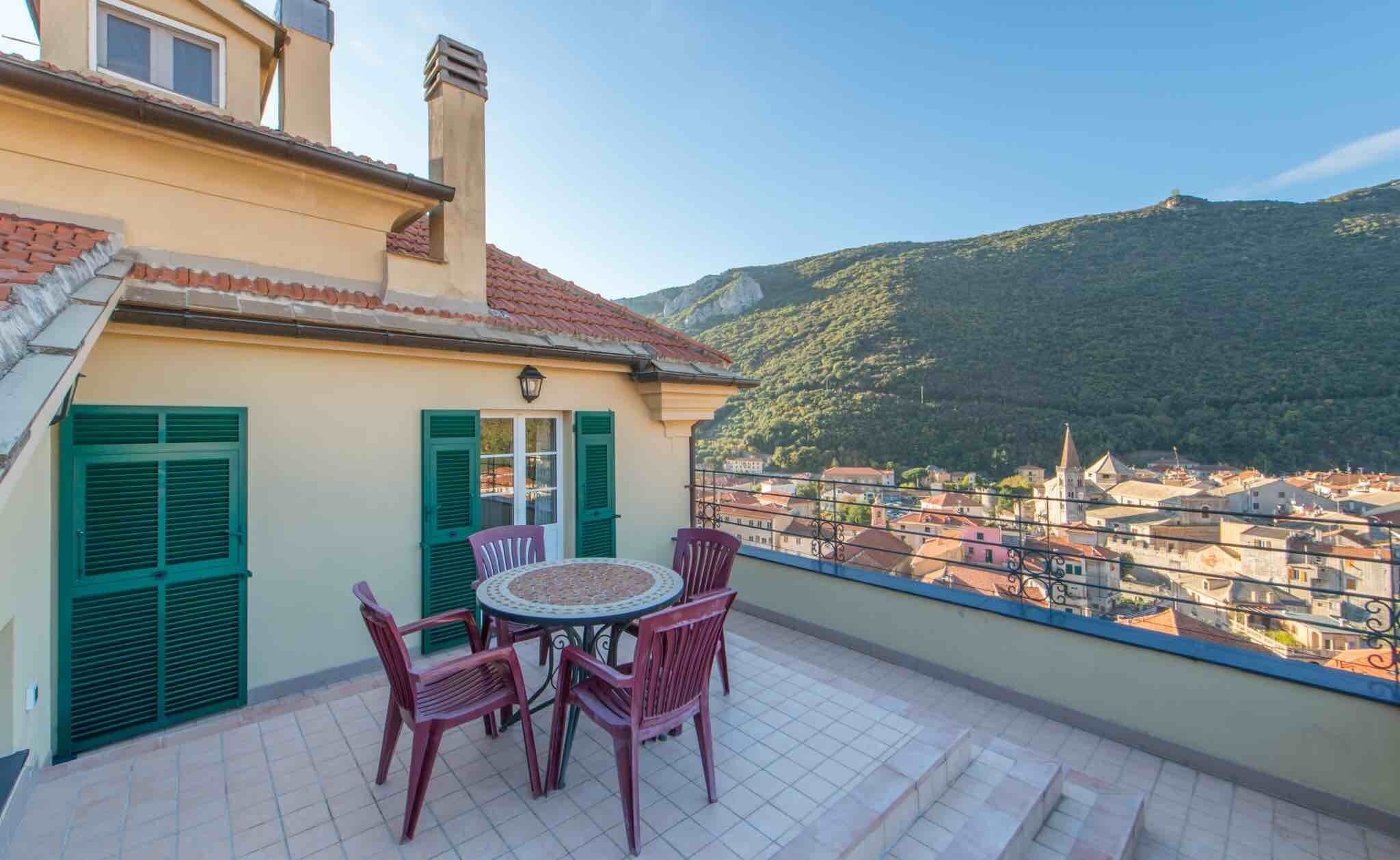 Ein Balkon mit Tisch und Stühlen, mit Blick auf eine Stadt und Berge.