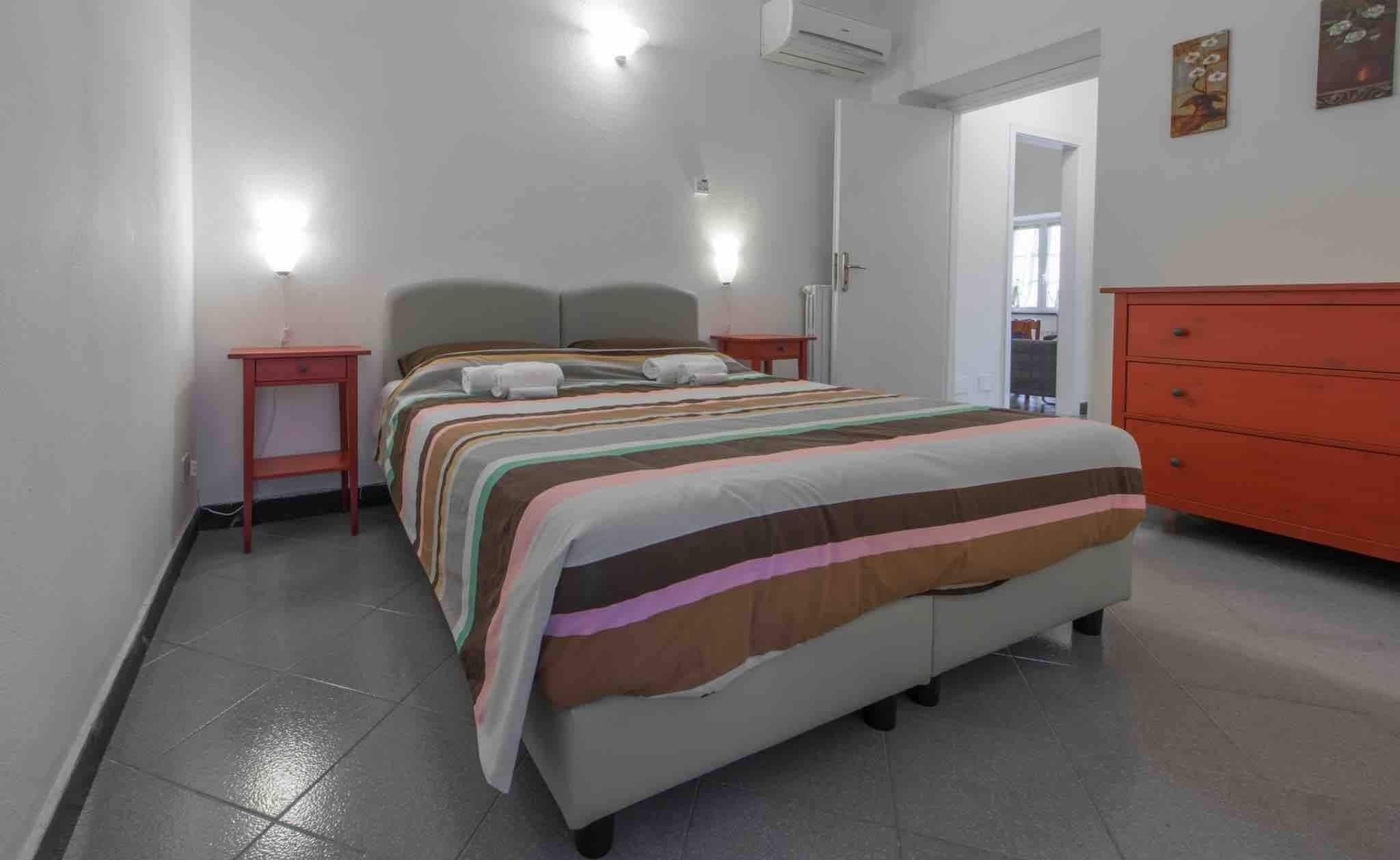 A bedroom with a bed, a nightstand, a dresser, and a door leading to another room.