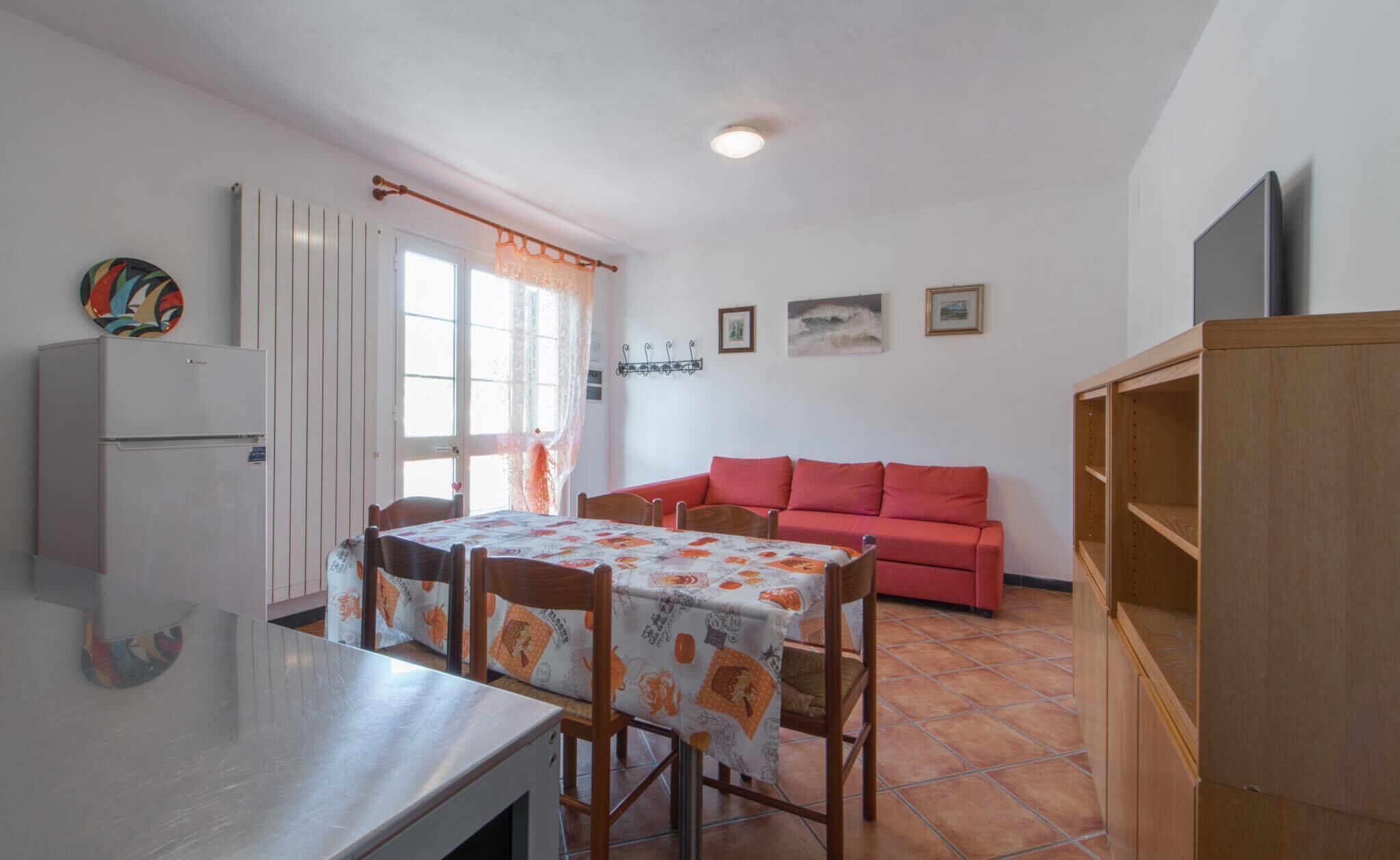 Un espacio habitable compacto con comedor, un sofá rojo, una pequeña cocina y un televisor.
