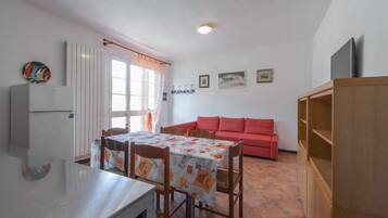 Un espacio habitable compacto con comedor, un sofá rojo, una pequeña cocina y un televisor.