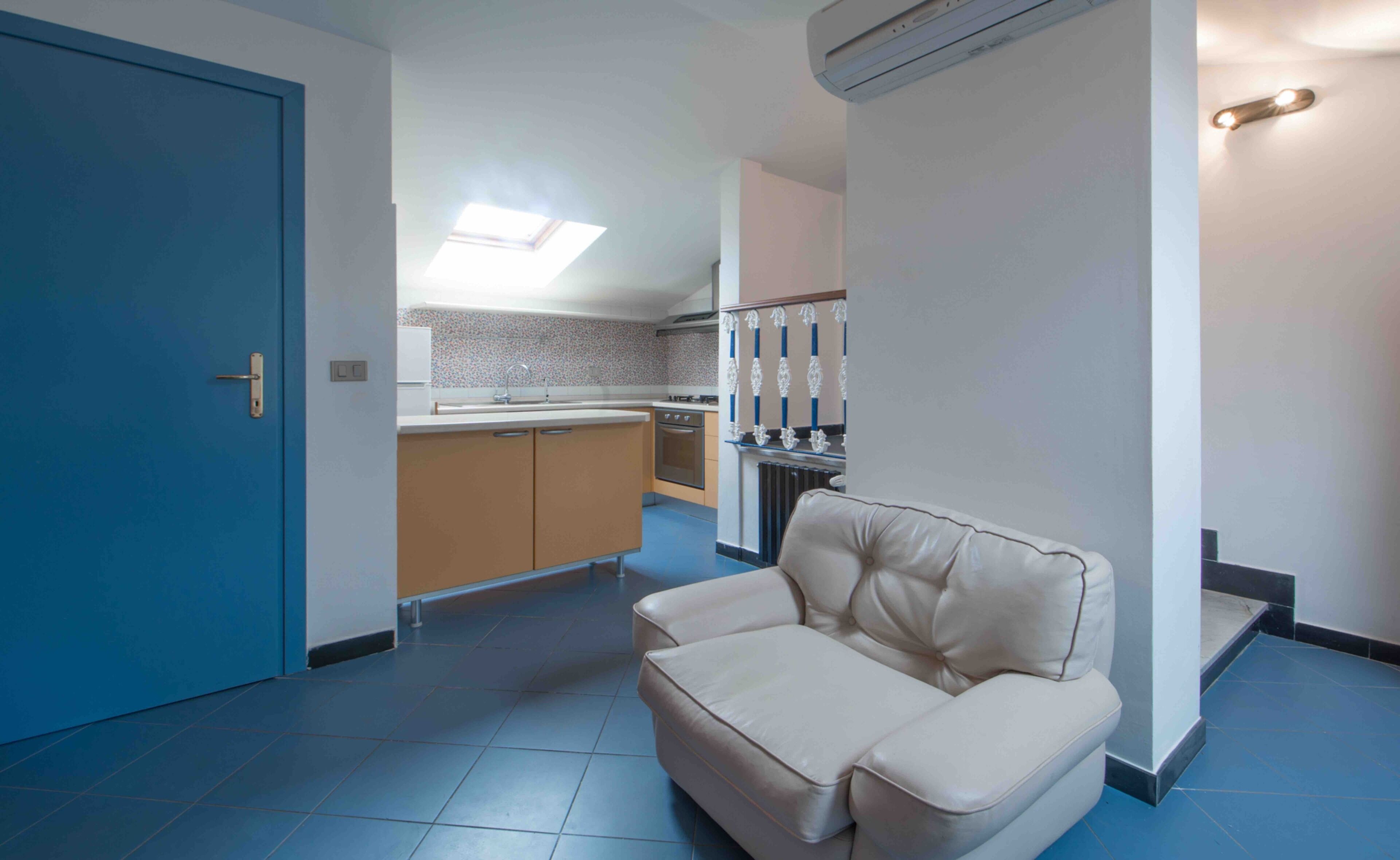 A modern kitchen with a skylight, a beige sofa, and a blue door.