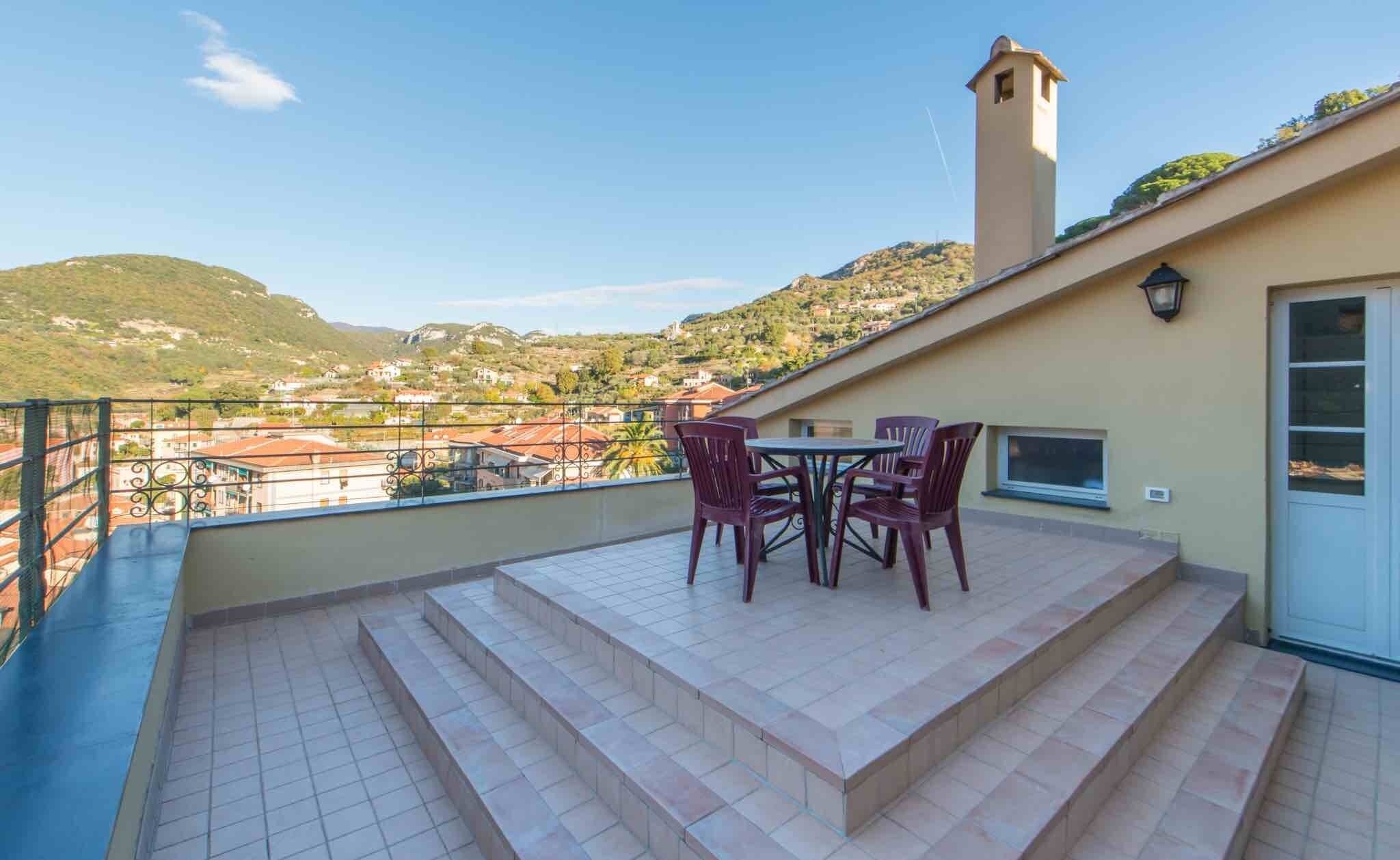 Een terras met een tafel en stoelen, een klein torentje en uitzicht op een heuvelachtig stadje.