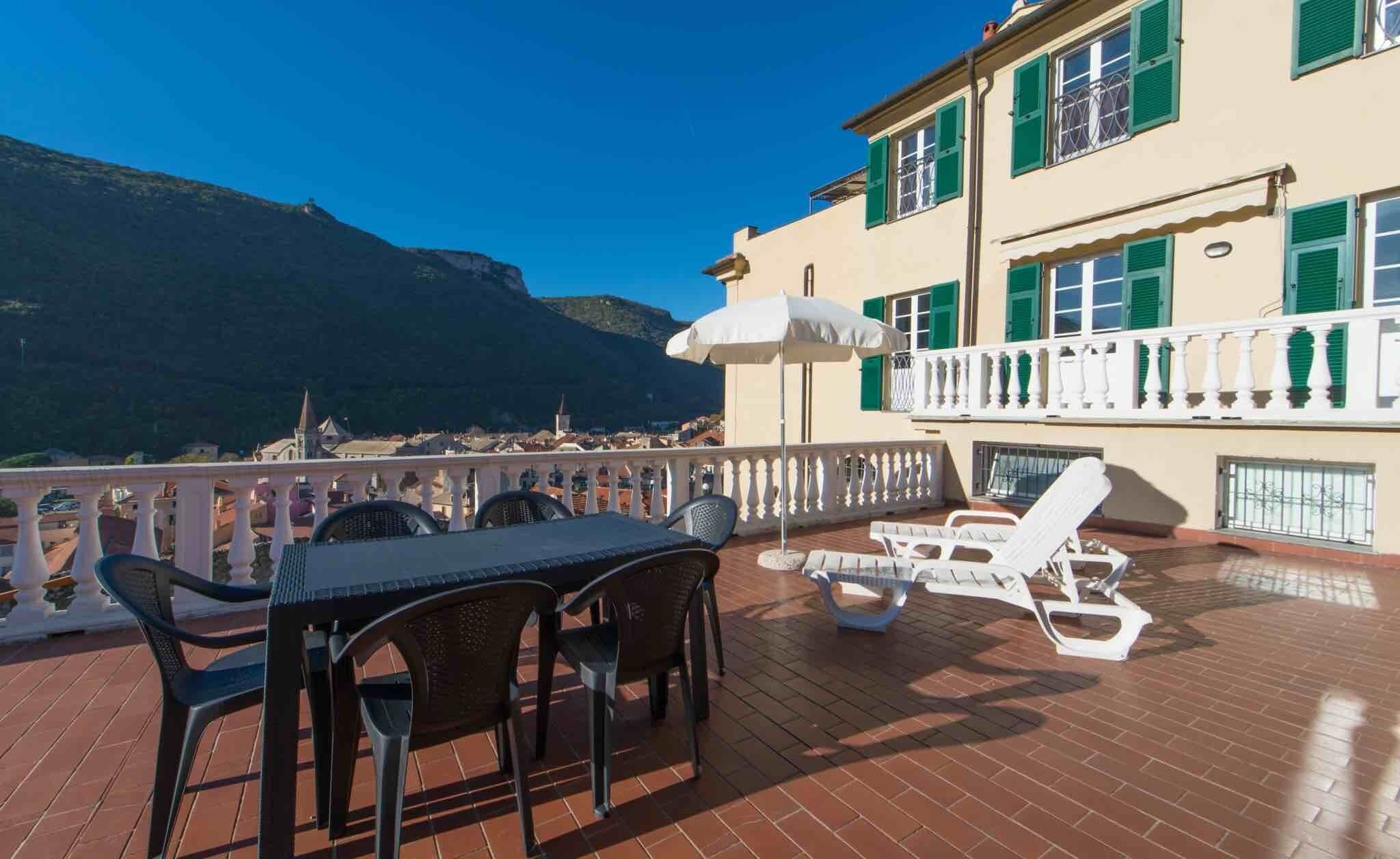 A terrace with a table and chairs, a sun umbrella, and a view of a mountain and town.