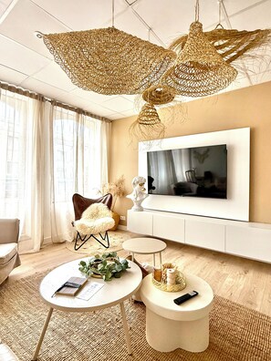 Ein modernes Wohnzimmer mit einem großen Flachbildfernseher an der Wand, einem bequemen Ledersessel, einem runden Couchtisch und einer ungewöhnlichen, gewobenen Leuchte.