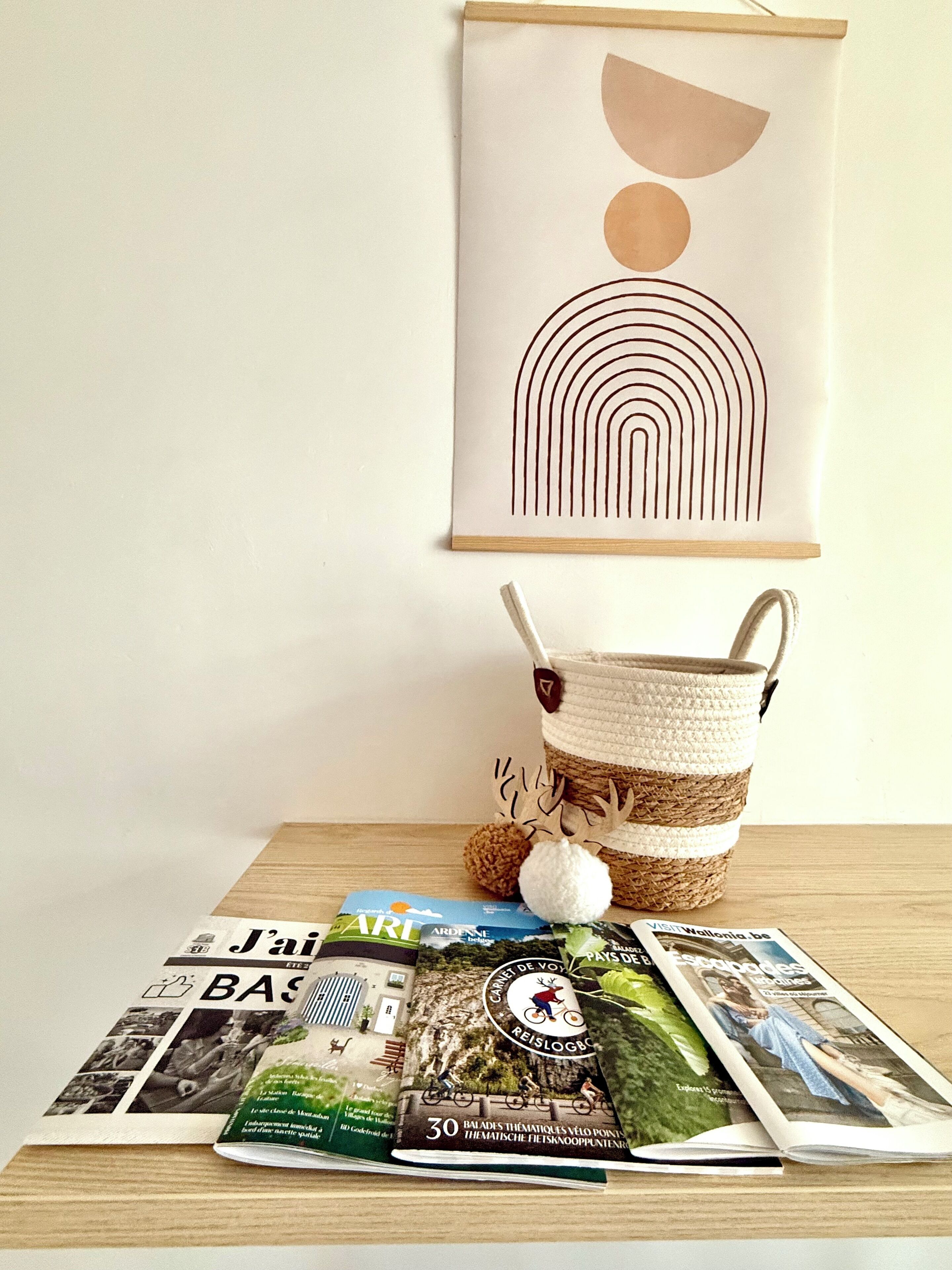A wooden table with a woven basket, a framed abstract artwork, and several travel brochures.