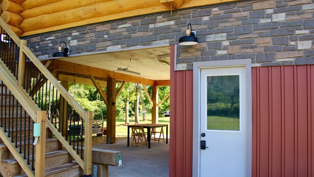 A covered outdoor area with a wooden staircase, a stone wall, and a red door. - Custom Log Home directly along the Greenbrier River sits the River Ridge Retreat (Marlinton)