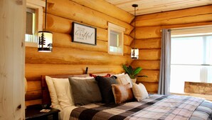 A log cabin bedroom with a bed, nightstands, a framed quote on the wall, and a window with curtains. - Custom Log Home directly along the Greenbrier River sits the River Ridge Retreat (Marlinton)