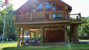 A two-story log cabin with a balcony, a covered porch, and a flagpole. - Custom Log Home directly along the Greenbrier River sits the River Ridge Retreat (Marlinton)