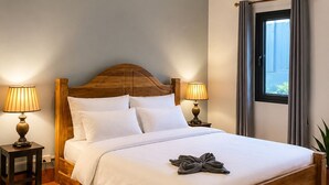 Habitación de hotel con cama de madera, dos lámparas de noche, ventilador de techo, equipo de aire acondicionado, ventana con cortinas y alfombra geométrica.