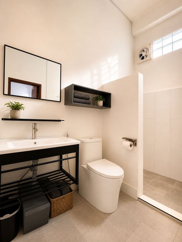 Un baño moderno con lavamanos, espejo, inodoro y ducha blancos.
