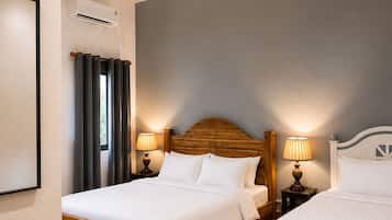 A hotel room with two beds, a ceiling fan, bedside lamps, a potted plant, and a blue rug.