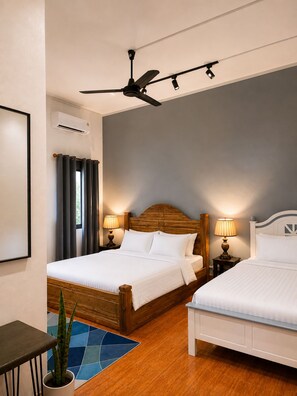 Een hotelkamer met twee bedden, een plafondventilator, bedlampjes, een potplant en een blauw vloerkleed.