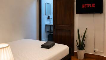 Ein Hotelzimmer mit einem Bett, einer Nachttischlampe, einem an der Wand montierten Fernseher und einer Zimmerpflanze.