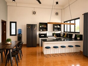 A modern kitchen with a central island, bar stools, a dining table, and a water dispenser.