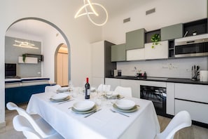 Une cuisine moderne avec des meubles blancs, un four encastré et un coin repas agrémenté d’une table blanche dressée pour le repas.