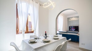 Een eethoek met een tafel gedekt voor vier personen, een wijnfles en een televisie op de achtergrond.