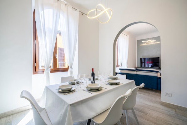 A dining area with a table set for four, a wine bottle, and a television in the background.