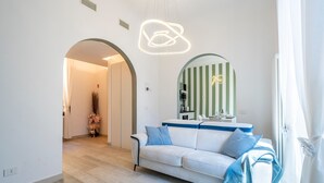 Een moderne woonkamer met een witte bank, een blauwe plaid, een spiegel met groene strepen en een bijzondere plafondlamp.
