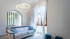 Een moderne woonkamer met een bank, een ronde spiegel, een tafel met een lamp en twee voetenbankjes.