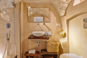 Ein Badezimmer mit Duschkabine aus Glas, einem weißen Waschbecken mit Marmorplatte, einem Spiegel über dem Waschbecken und einem gewebten Korb auf einem Holzschemel.