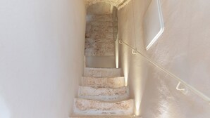 Un escalier, avec un mur de pierre d’un côté et un mur blanc de l’autre, qui mène à l’étage supérieur.