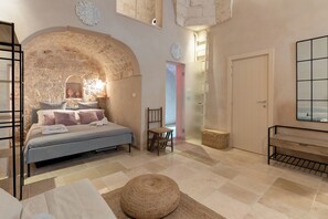 Ein Schlafzimmer mit Steingewölbe, einem Bett, einem Sessel, einer Bank und einem großen Spiegel.