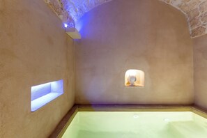 A spa room with a bathtub, a small window, and a stone wall.