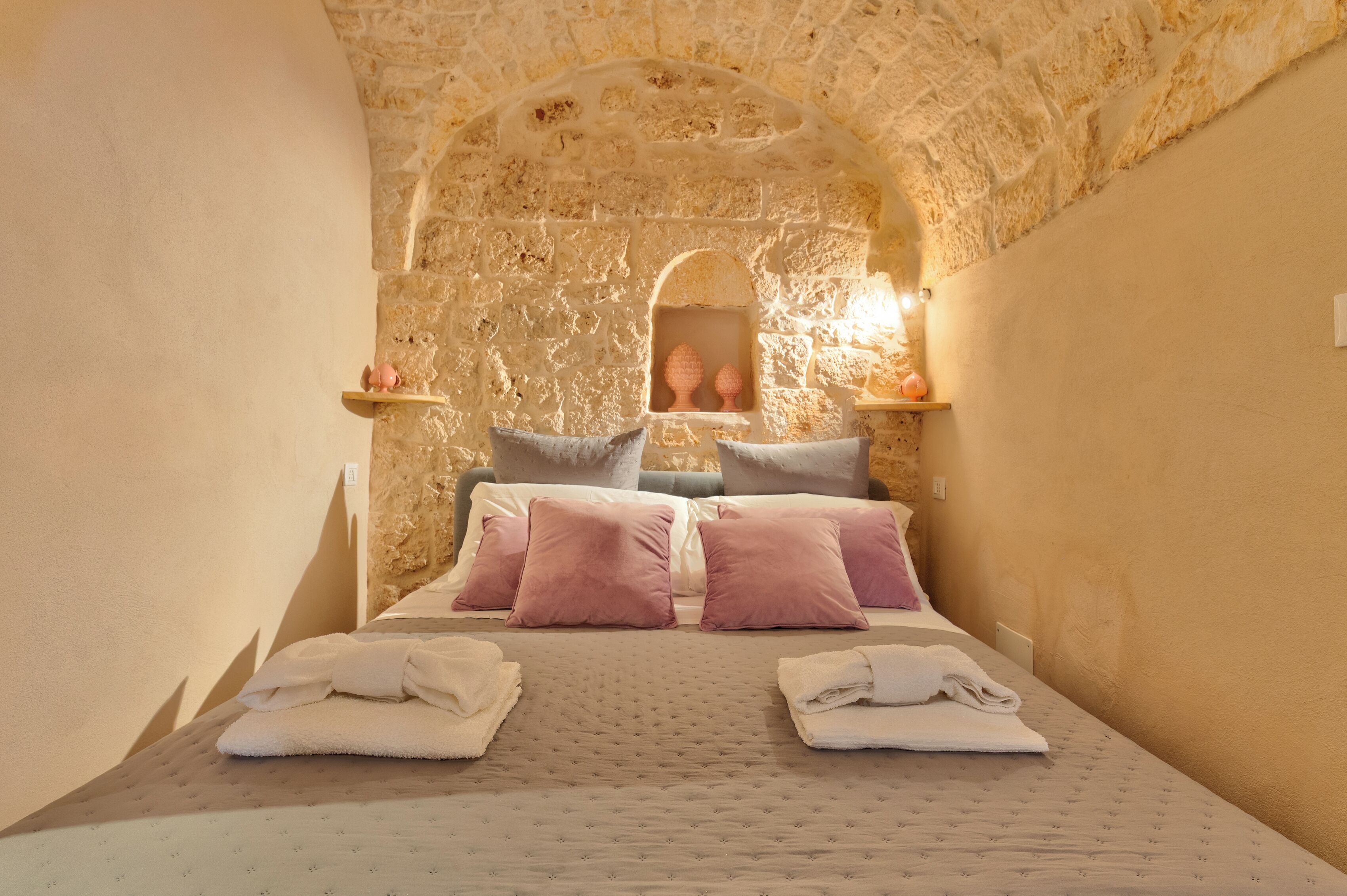 A bedroom with a stone wall, a bed with pillows, and a mirror.