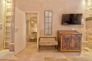 A room with a wooden cabinet, a TV mounted on the wall, a bench, and a ladder.