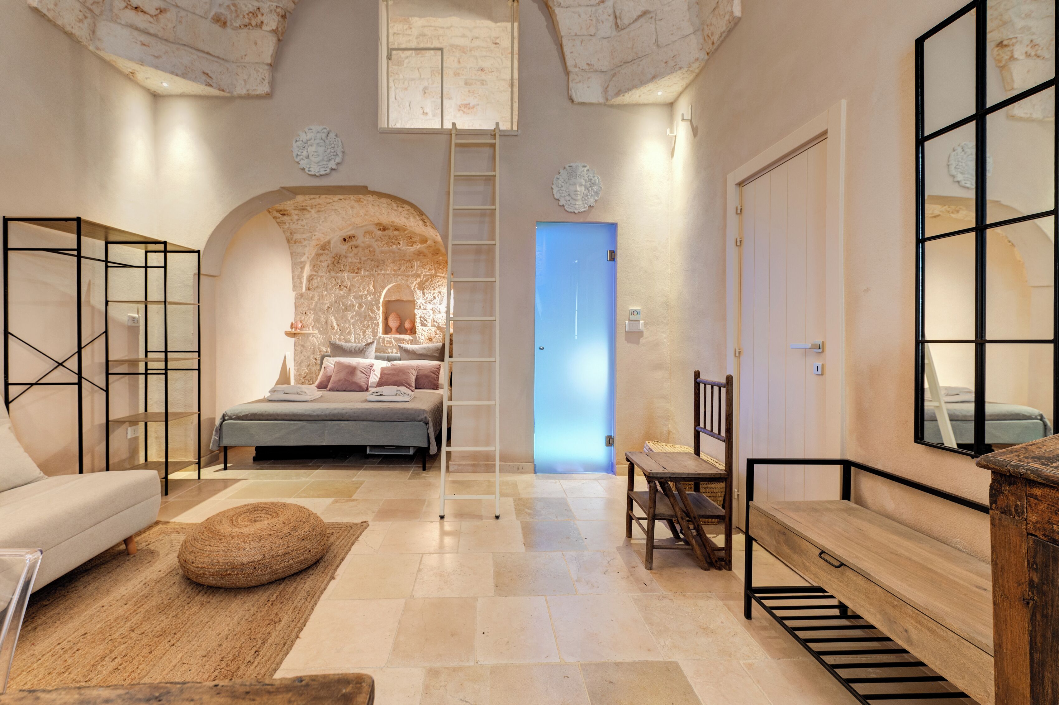 Una camera da letto con parete in pietra, un letto, una panca di legno e una scala.