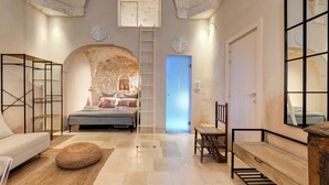 Une chambre avec un mur en pierre, un lit, un banc en bois et un escalier.