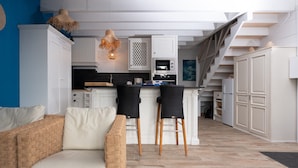 A modern kitchen with white cabinetry, a dining area with two black chairs, and a staircase leading to an upper level.