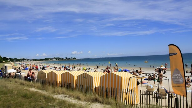A beach with rows of yellow striped beach huts, a clear sky, and the ocean in the background.