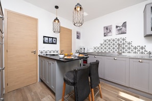 Una cocina moderna con armarios grises, una puerta de madera, dos sillas de mimbre e iluminación colgante.