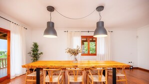 A dining area with a wooden table and chairs, pendant lights, a vase with flowers, and a window with curtains. - Villa 'Tramuntana' with Sea View, Wi-Fi and Air Conditioning (Costa d'en Blanes)