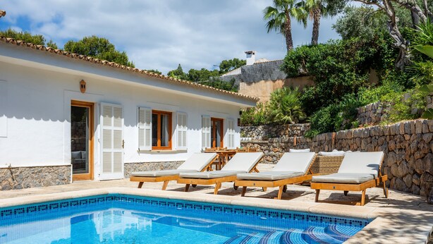 A swimming pool with lounge chairs, a stone wall, and a white building with shutters. - Villa 'Tramuntana' with Sea View, Wi-Fi and Air Conditioning (Costa d'en Blanes)