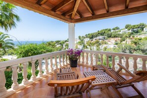A balcony with wooden furniture and a potted plant, overlooking a coastal town. - Villa 'Tramuntana' with Sea View, Wi-Fi and Air Conditioning (Costa d'en Blanes)