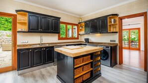 A modern kitchen with dark cabinets, a central island, a washing machine, and a view of the outdoors. - Villa 'Tramuntana' with Sea View, Wi-Fi and Air Conditioning (Costa d'en Blanes)