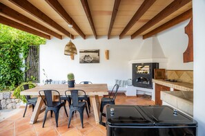 An outdoor patio with a wooden table and chairs, a grill, and a hanging light fixture.