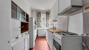 A narrow kitchen with white cabinets, a wooden countertop, a stove, and a window with patterned curtains. - Śródmieście Apt -Balcony, Workspace - by Rentujemy (Warszawa)
