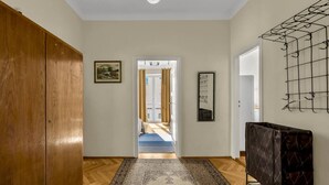 A hallway with a wooden wardrobe, a patterned rug, a framed picture, a mirror, and a radiator. - Śródmieście Apt -Balcony, Workspace - by Rentujemy (Warszawa)