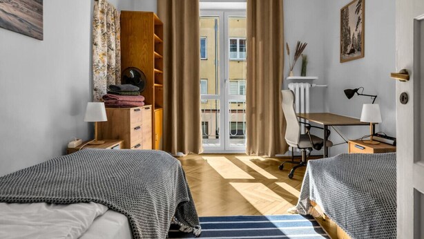 A hotel room with two beds, a desk, a chair, a wardrobe, and a view of the outside. - Śródmieście Apt -Balcony, Workspace - by Rentujemy (Warszawa)