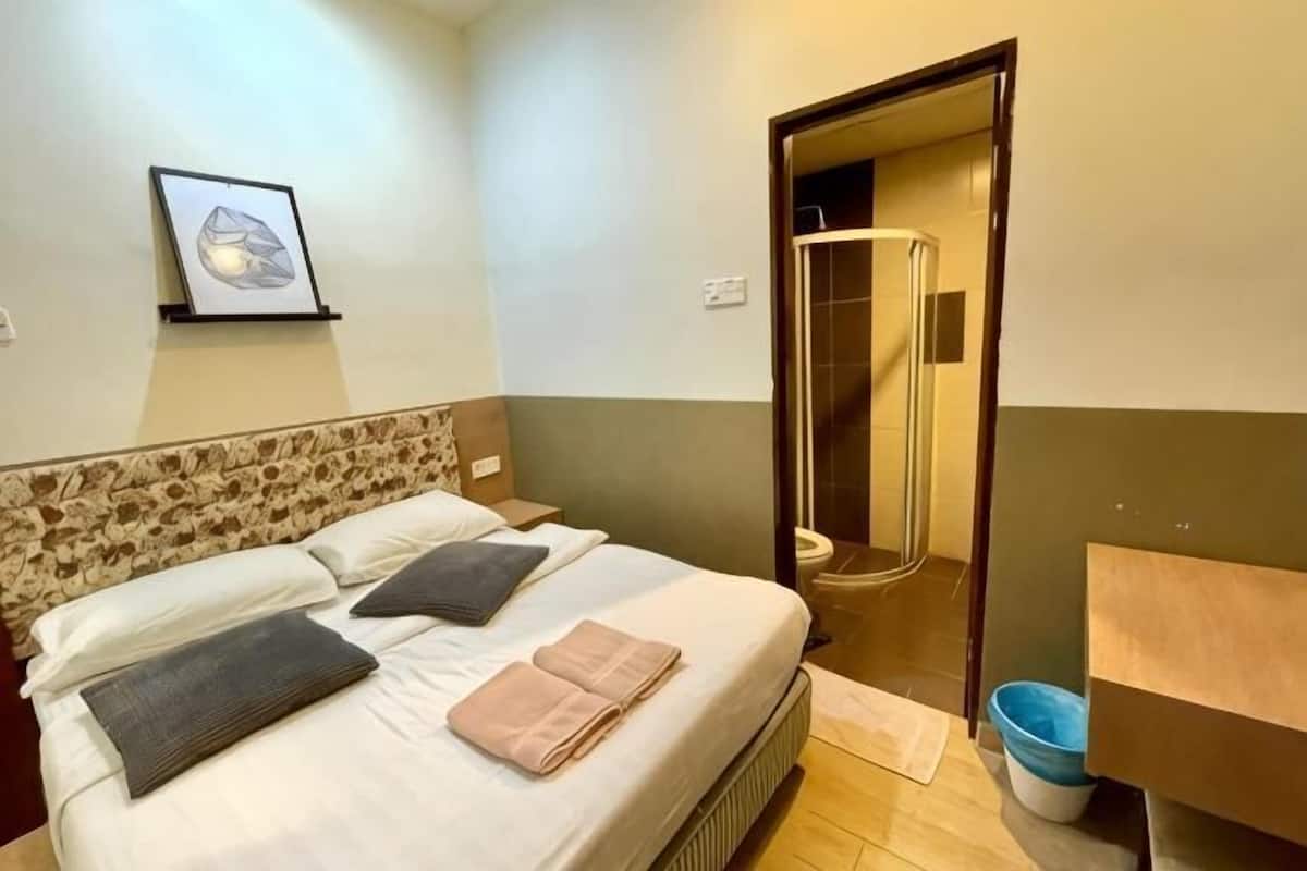 A bedroom with a bed, a headboard, a framed picture on the wall, and a bathroom visible through an open door.