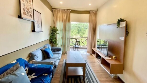 A modern living room with a sofa, a coffee table, a TV, and a balcony with a view. - PLAY at Iris Resort Tanah Rata (Cameron Highlands)