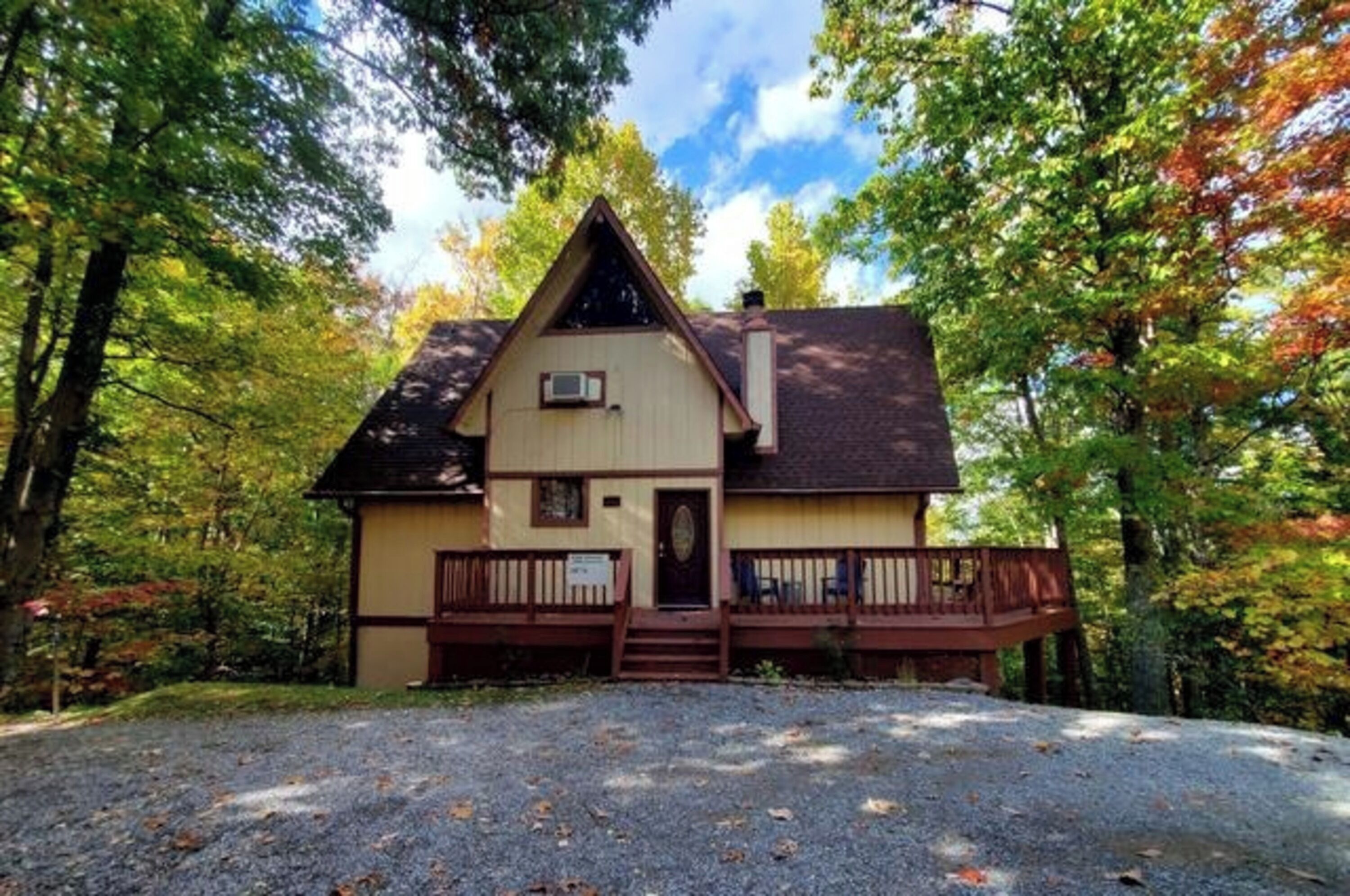 A two-story cabin with a front porch, surrounded by trees.