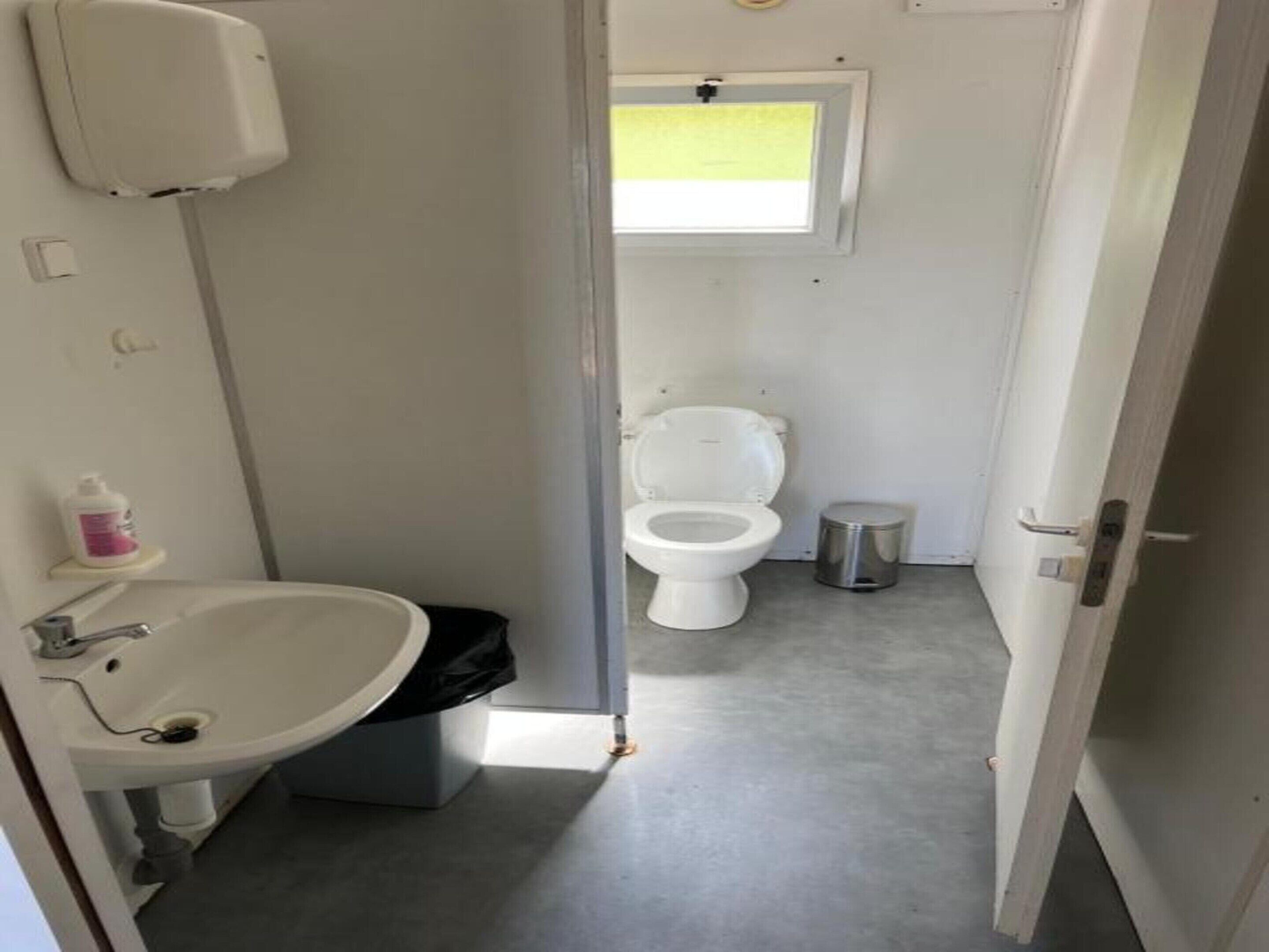 A small, compact bathroom with a white sink, toilet, and trash bin.