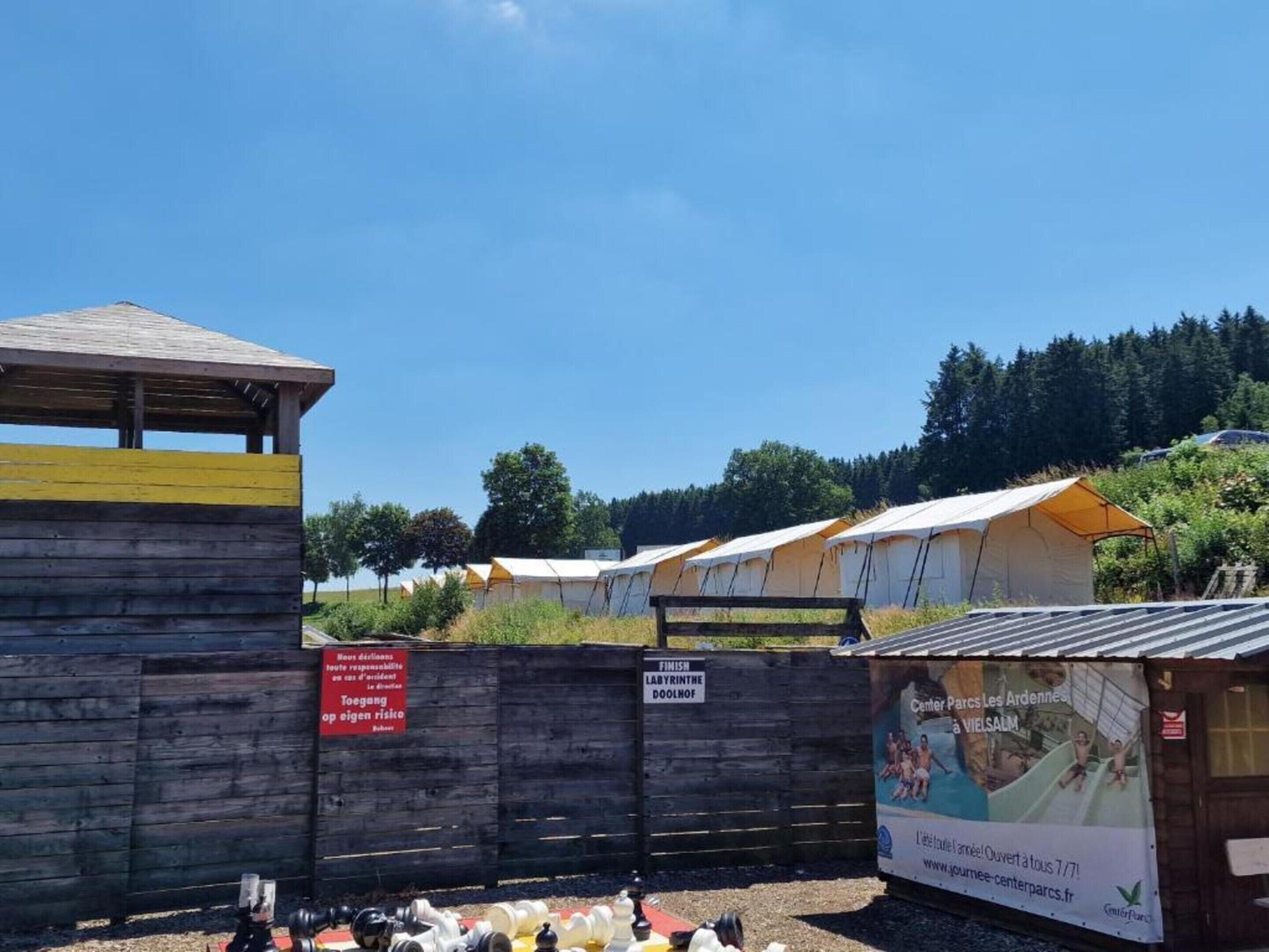 A wooden structure with a yellow stripe, a sign indicating a finish, and a tent-like building with a sign in the background.