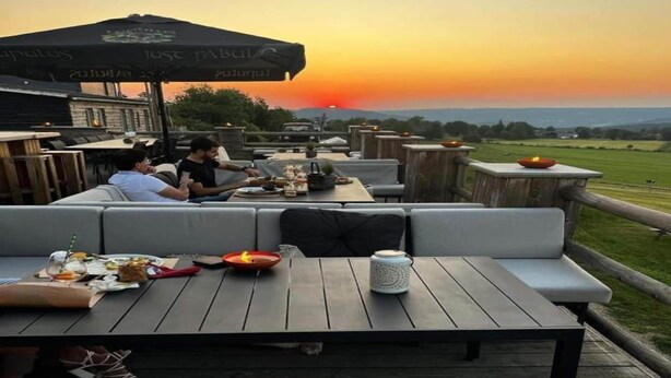 An outdoor dining area with wooden tables and benches, a sunset view, and a casual atmosphere. - Nature Escape Tent at Val de Wanne (Trois-Ponts)