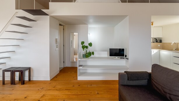 A modern interior with a staircase, a flat-screen TV, a plant, and a kitchen area.