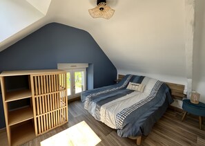 A bedroom with a sloped ceiling, a bed with patterned bedding, a wooden wardrobe, and a small bedside table.